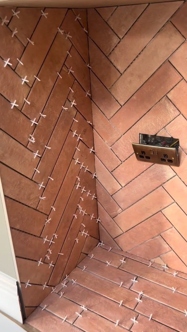 Herringbone tiles going up round a fireplace, spacers still in