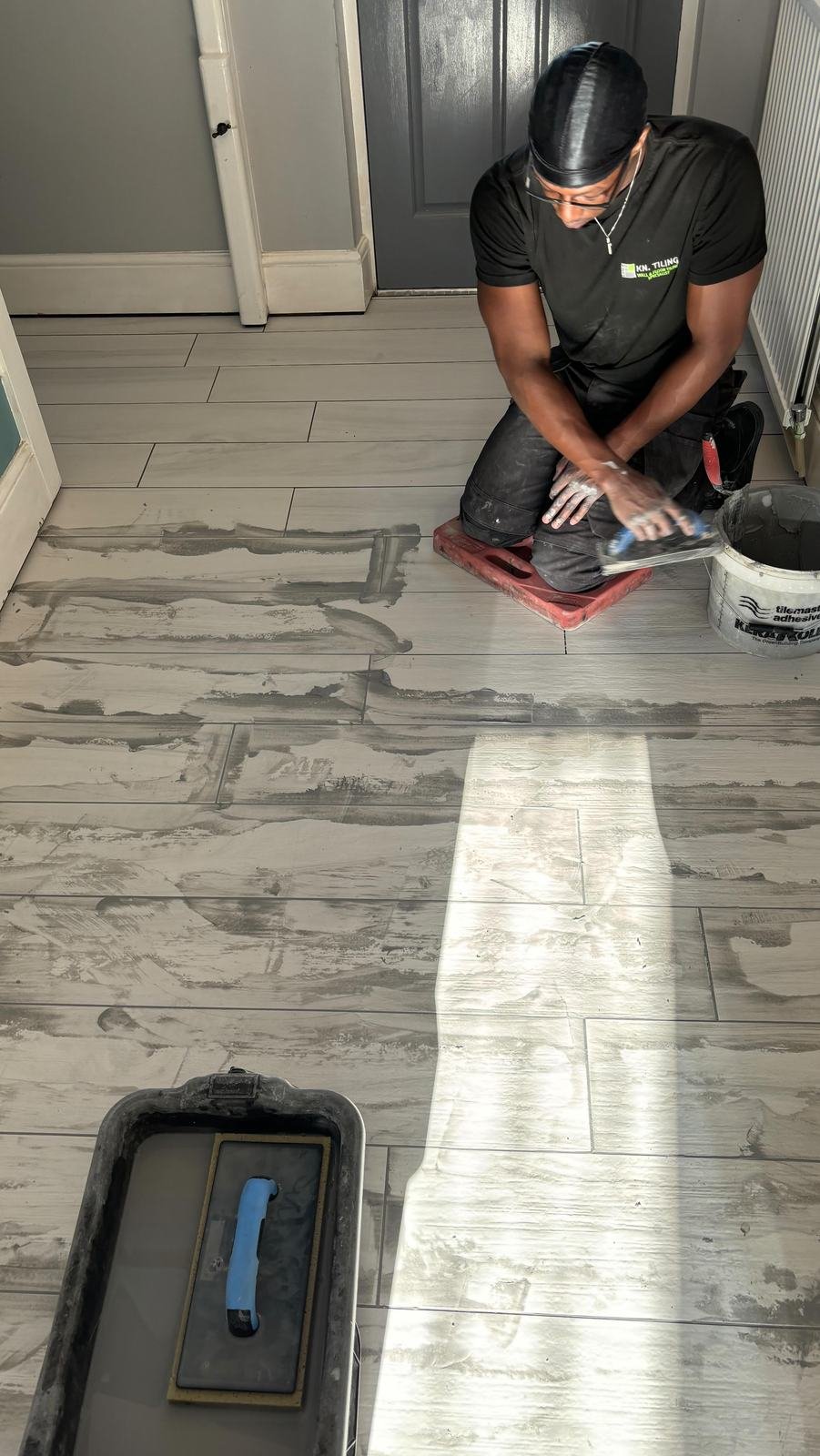 A Kn.tiling tiler laying wood-effect tiles through a hallway, with a laser line on the floor