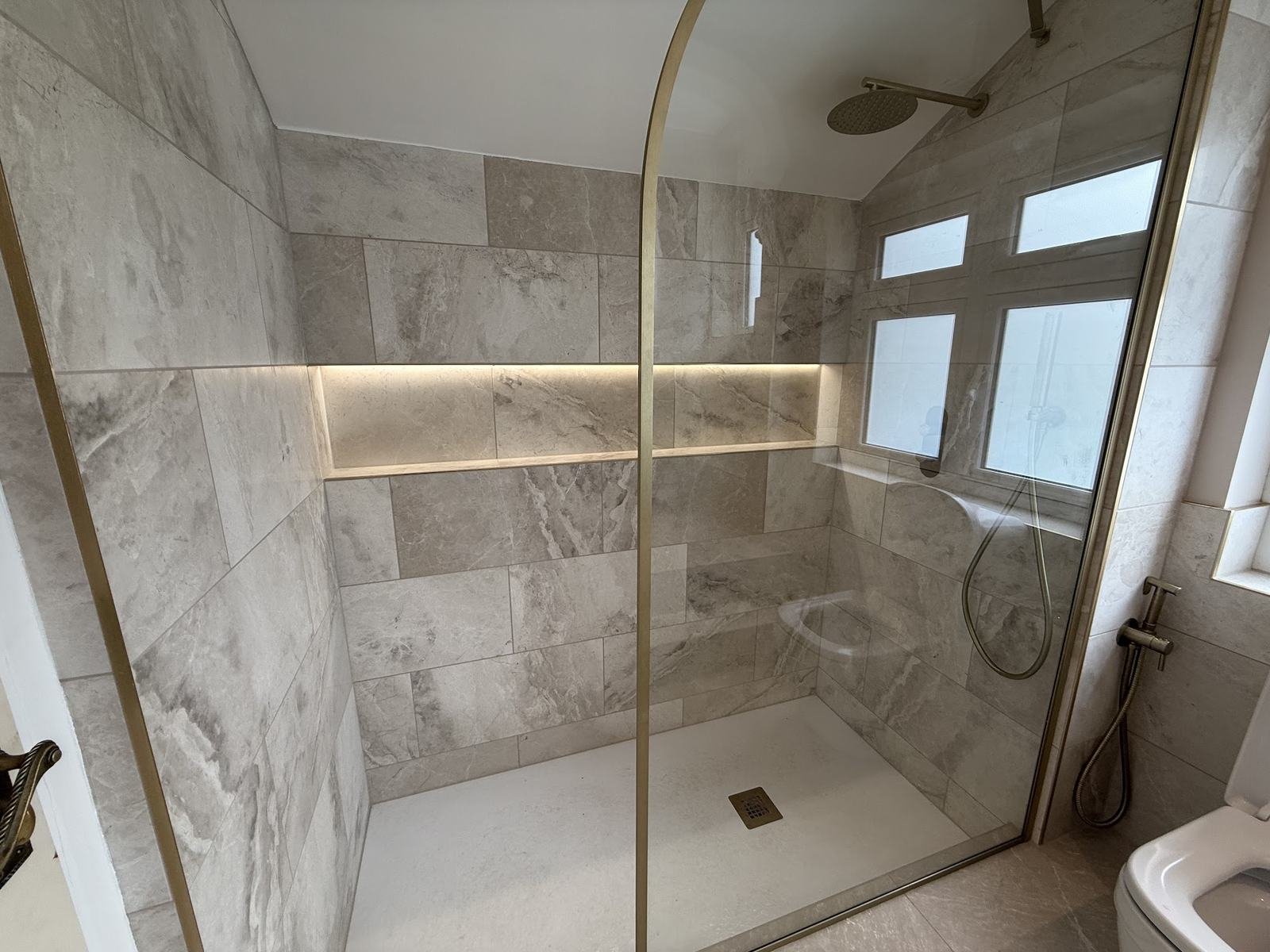 Walk-in shower in large marble-effect tiles with a lit full-width niche